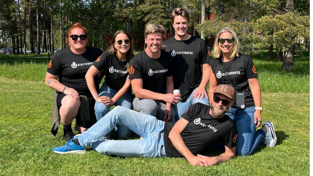 Arbeta med employee advocacy och gör dina anställda till varumärkesamnbassadörer. Digitrooperteamet är uppställda som ett fotbollslag i det gröna gräster. De är iklädda sina svarta t-shirtar med Digitrooper logga på bröstet.